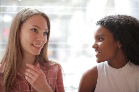 Two women smiling and talking indoors, expressing friendship and happiness.
