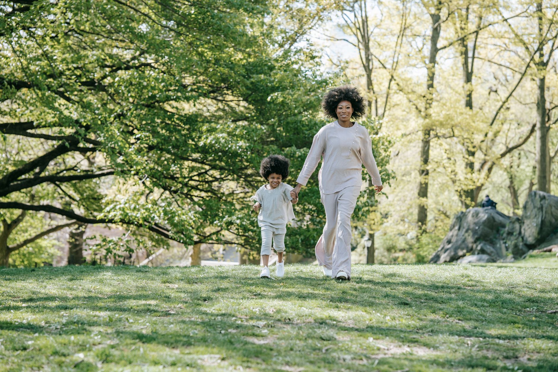Une femme et un jeune enfant marchent main dans la main sur une pelouse bordée d’arbres.